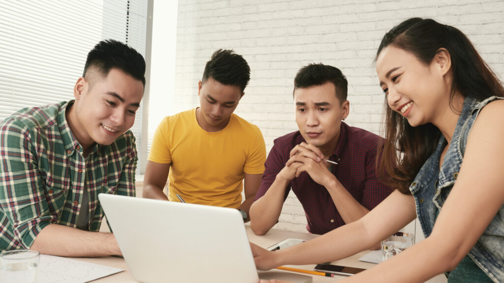 Tim digital marketing sedang berdiskusi di depan laptop, membahas website beli putus dan website berlangganan.