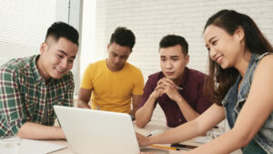 Tim digital marketing sedang berdiskusi di depan laptop, membahas website beli putus dan website berlangganan.