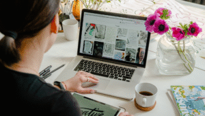 Seorang wanita sedang mencari inspirasi desain visual di Pinterest uuntuk kebutuhan bisnis melalui laptop, sambil memegang tablet bertuliskan “creative”, menunjukkan aktivitas branding digital yang bergantung pada media sosial.
