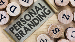 Teks "Personal Branding" tercetak tebal di atas gulungan kertas coklat, dikelilingi keping kayu bertuliskan huruf-huruf alfabet, menggambarkan konsep identitas dan komunikasi personal.