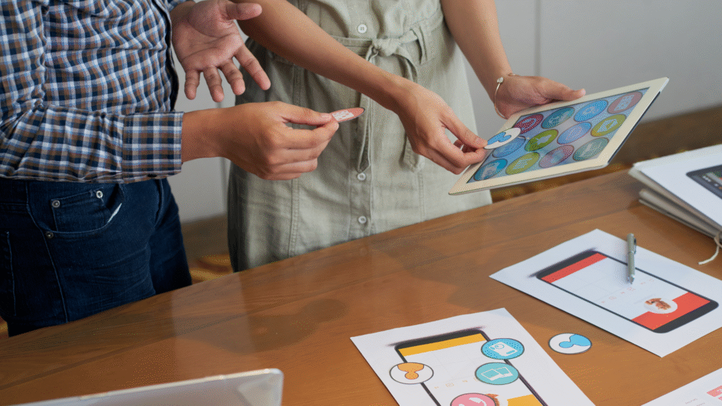 Dua orang mendiskusikan elemen desain antarmuka pengguna (UI) website menggunakan tablet dan mockup, merepresentasikan proses branding digital. Dua orang mendiskusikan elemen desain antarmuka pengguna (UI) website menggunakan tablet dan mockup, merepresentasikan proses branding digital.