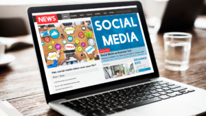 Tampilan layar laptop menampilkan halaman berita online bertema "Social Media" dan artikel terkait penggunaan media sosial dalam bisnis.