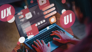 Tangan sedang mengetik di laptop dengan visual elemen UI dan UX yang melayang di layar, merepresentasikan proses desain antarmuka pengguna dan pengalaman pengguna dalam pengembangan website atau aplikasi digital.