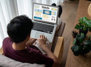 Pria sedang merancang tampilan website di laptop sambil duduk santai di ruang kerja rumah, mencerminkan pentingnya memiliki situs web untuk bisnis modern.